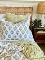 Bed with patterned bedding and pillows, nightstand with lamp and plant, wicker headboard.