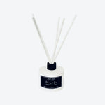 A reed diffuser bottle with a white glass container, a black cap, and four white reeds, featuring a black label with white text that reads 'LUNA BLU' and 'Scented Oil'.