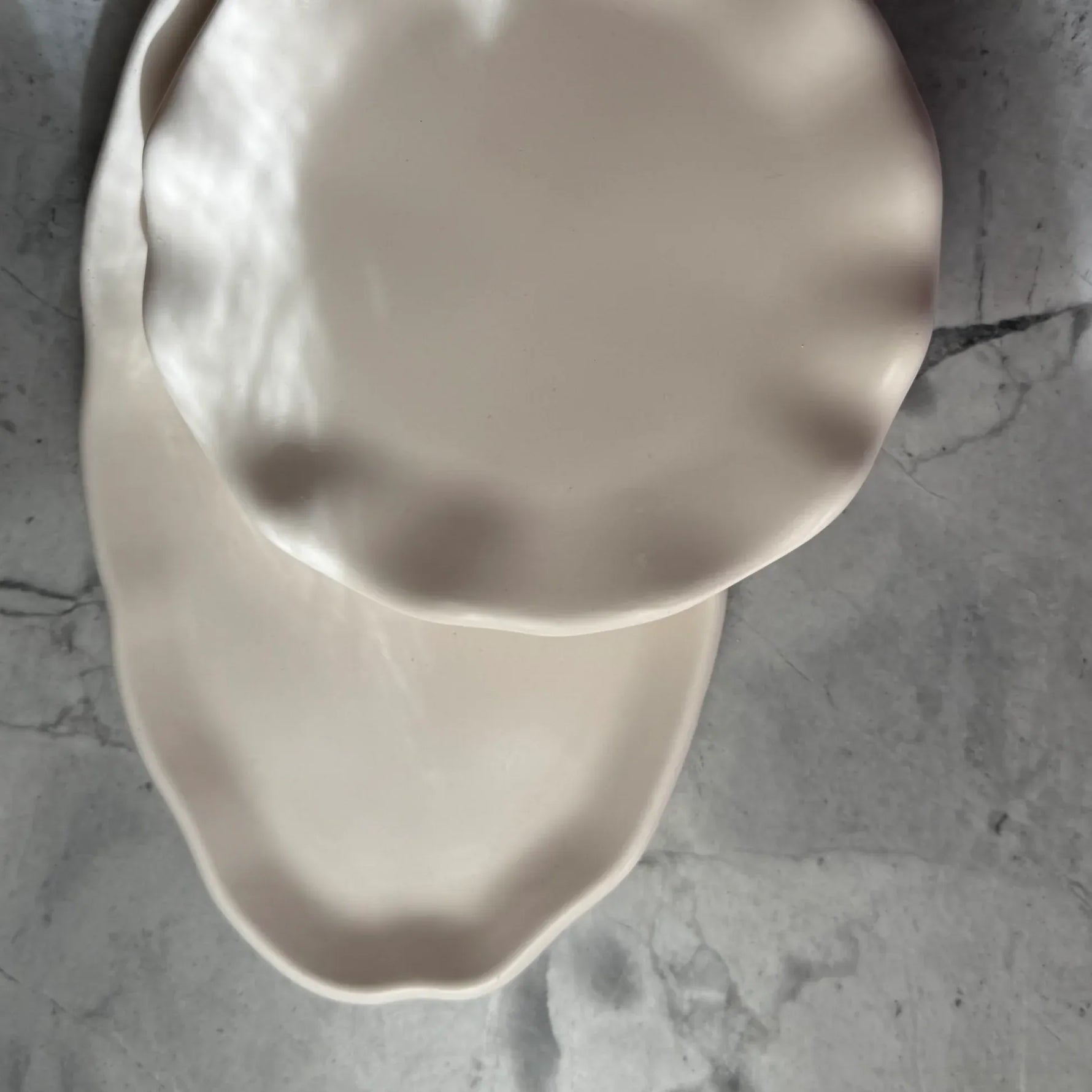 Two scalloped-edge ceramic plates in a warm cream color, stacked on a gray marble surface.