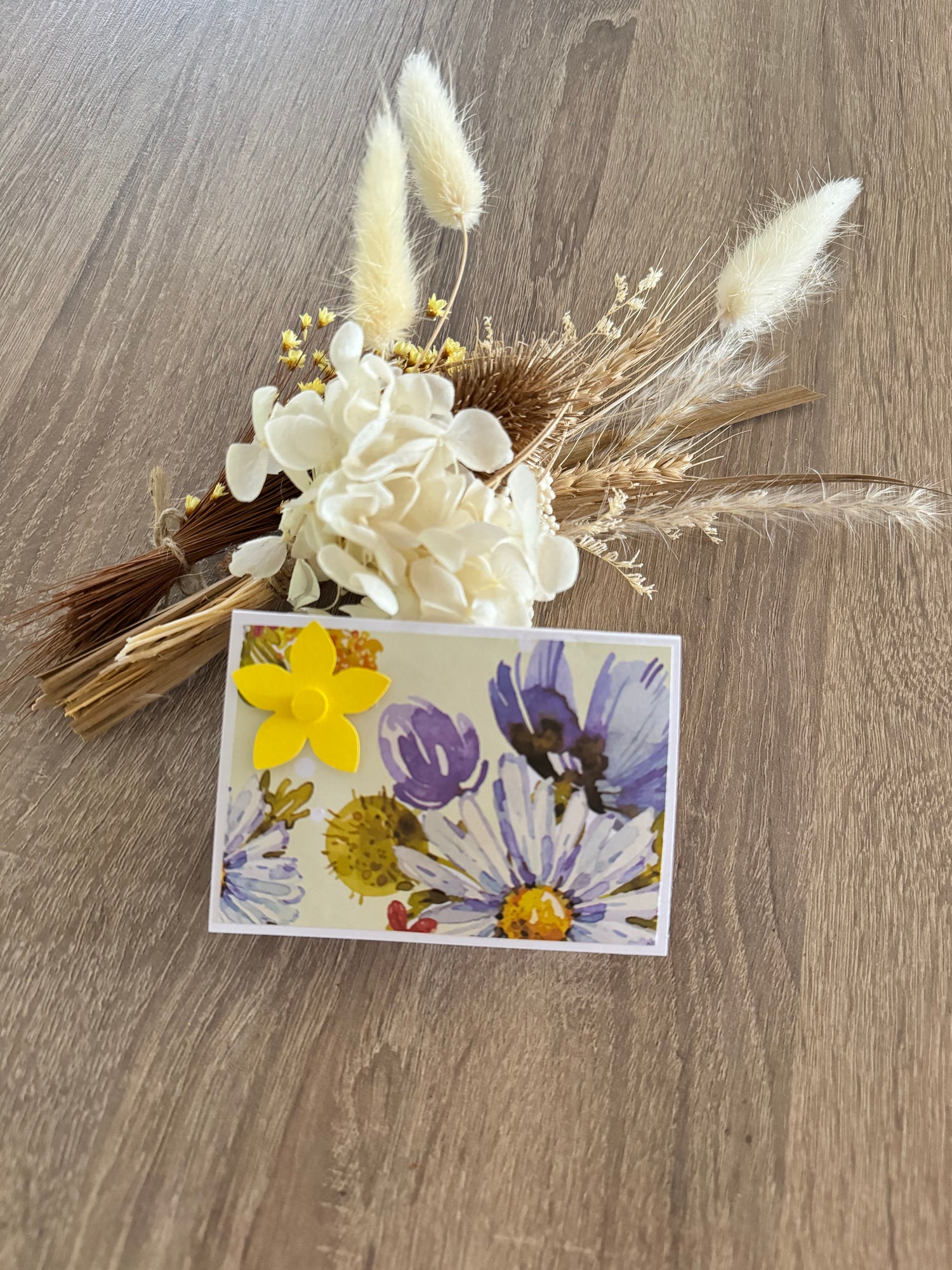 Floral arrangement with a card featuring floral design on a wooden surface