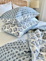 Floral patterned pillows and blanket on a bed with a wicker headboard.