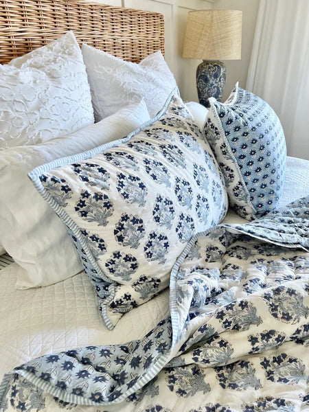 Floral patterned blanket draped over a bed with pillows and a lamp in the background.