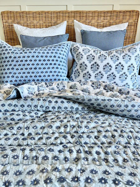 Bed with floral patterned bedding and pillows against a wooden headboard.