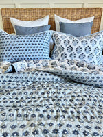 Bed with floral patterned bedding and pillows against a wooden headboard.