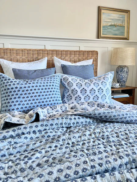 Bed with blue and white floral bedding, wicker headboard, and lamp in a bedroom setting.