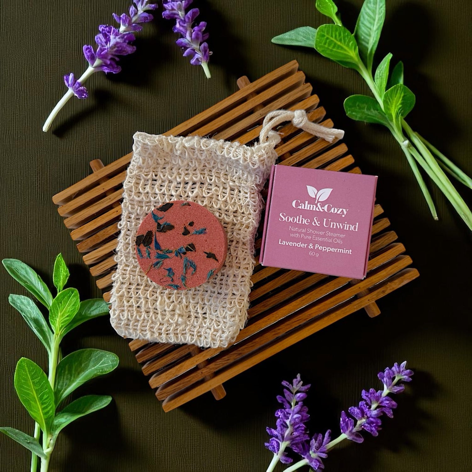 Beige soap in a mesh bag with a purple box labeled 'Calm & Cozy' on a dark surface with lavender flowers.