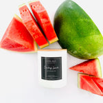 A white candle jar with a light wood lid and a black label reading 'LUNA BLU COLLECTION Sunday Lunch Watermelon' is styled with fresh watermelon slices and a whole watermelon on a white background.