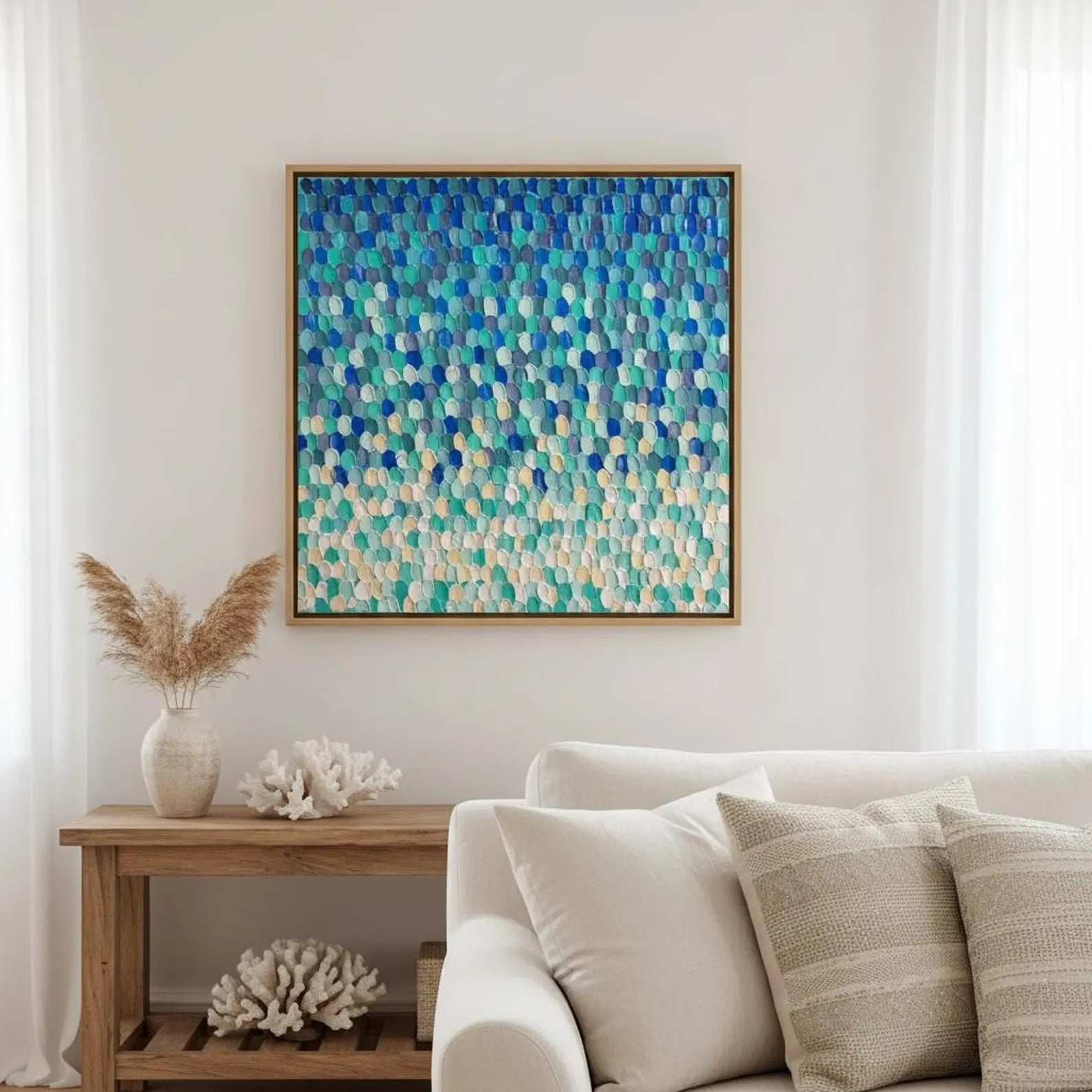 A square framed abstract canvas print featuring a textured mosaic of blue, teal, and cream geometric shapes, hanging on a white wall above a light beige sofa in a styled living room setting.
