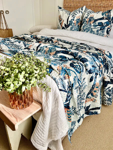Bed with floral bedding, pillows, and a plant on a wooden bench.