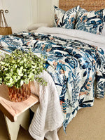 Bed with floral bedding, pillows, and a plant on a wooden bench.