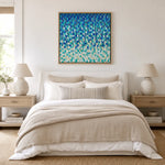 A framed abstract canvas print with textured blue, teal, and white brushstrokes hangs above a neatly made bed in a bright, modern bedroom with beige linens, matching nightstands, and lamps.