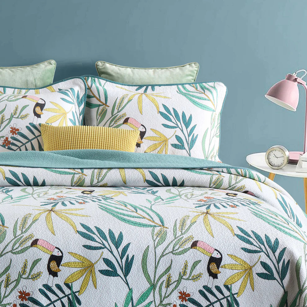 Tropical leaf and toucan patterned bedding set with pillows and a lamp on a blue background