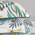 Floral and leaf patterned quilt with matching pillow on a gray background