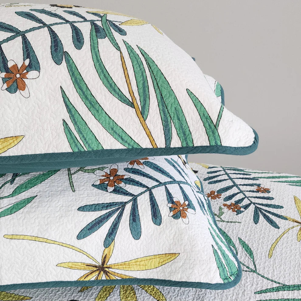 Floral and leaf patterned quilt with matching pillow on a gray background