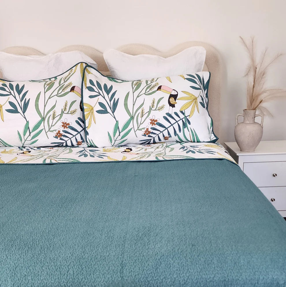 Bed with teal bedding and floral-patterned pillows in a bedroom setting.
