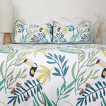 Tropical leaf and toucan patterned bedding set on a bed with a white headboard.
