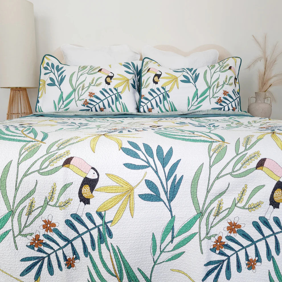 Tropical leaf and toucan patterned bedding set on a bed with a white headboard.
