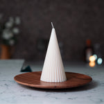 Conical white candle on a wooden plate with a blurred background