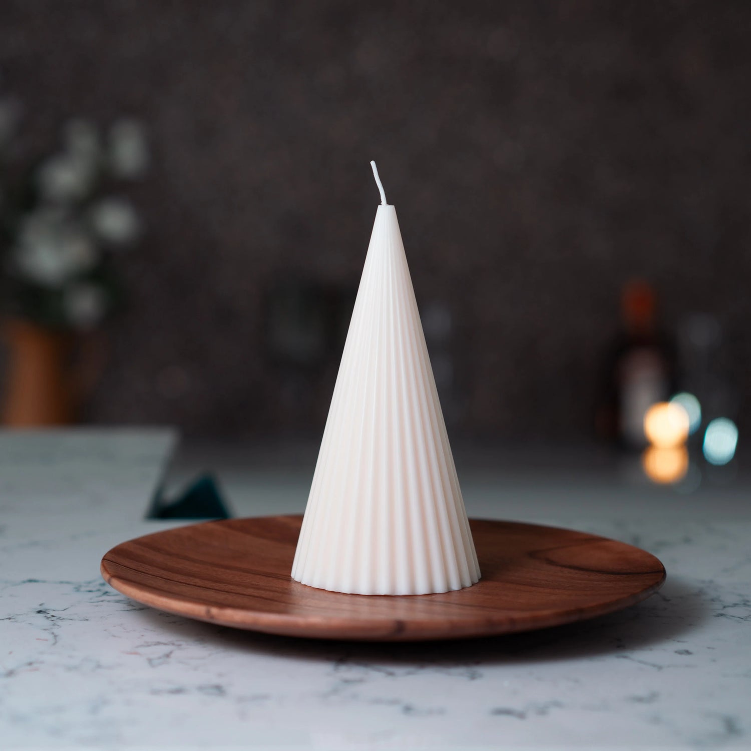 Conical white candle on a wooden plate with a blurred background