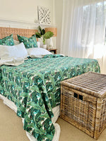 Bedroom with a bed covered in a green leaf-patterned comforter, wicker basket, and decorative pillows.