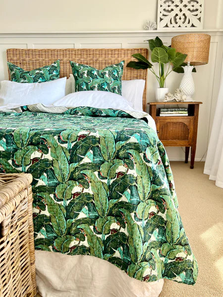 Bedroom with a bed covered in green leaf-patterned bedding, wicker headboard, and nightstand.