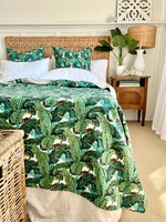 Bedroom with a bed covered in green leaf-patterned bedding, wicker headboard, and nightstand.