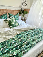 Bed with green leaf-patterned bedding and pillows in a bedroom setting.