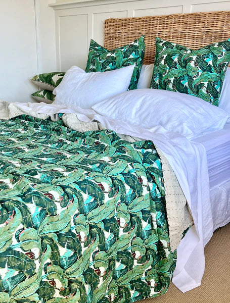 Bed with green leaf-patterned comforter and pillows in a bedroom setting