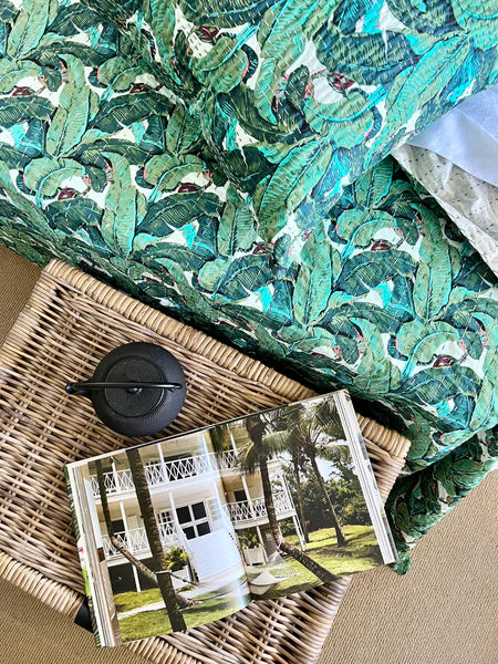 Green leaf-patterned fabric draped over a wicker basket with a card featuring a house and palm trees.