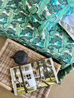 Green leaf-patterned fabric draped over a wicker basket with a card featuring a house and palm trees.