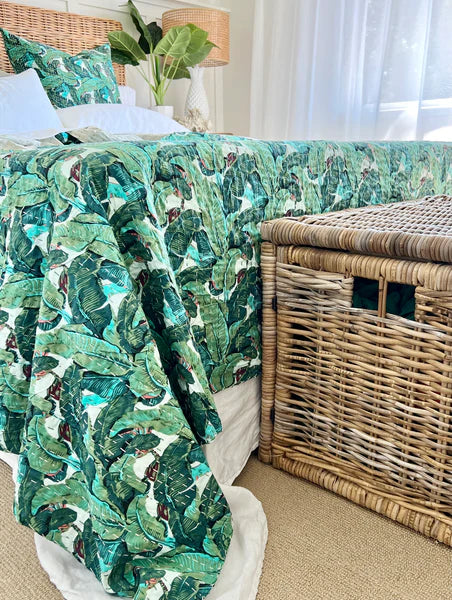 Bed with green leaf-patterned comforter next to a wicker basket in a room.