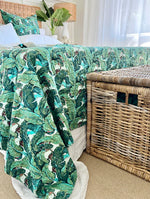 Bed with green leaf-patterned comforter next to a wicker basket in a room.