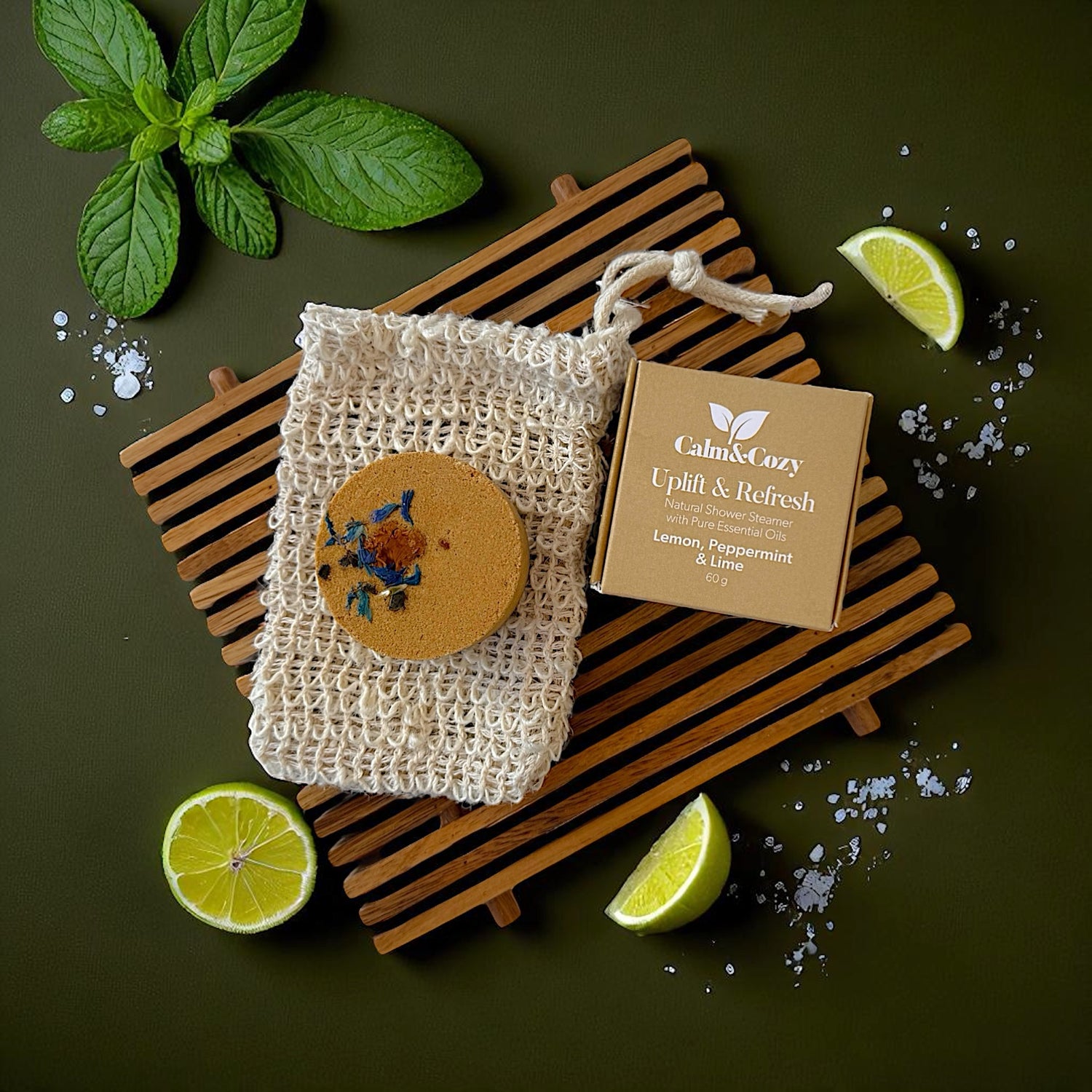 Soap bar in a mesh bag with a wooden disc on a wooden board, surrounded by lime slices and mint leaves on a dark background.