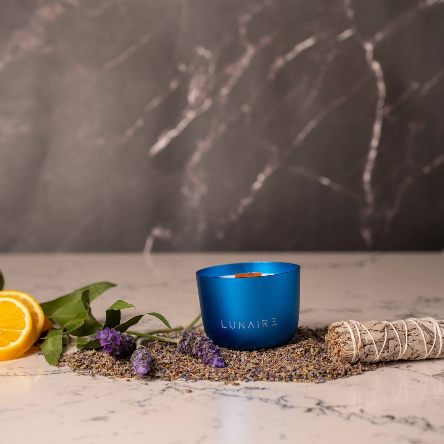 Blue candle labeled 'LUNAIRE' on a marble surface with lavender, orange, and sage.