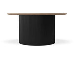 A modern round dining table featuring a fluted black pedestal base and a light brown wood top, shown against a plain white background.