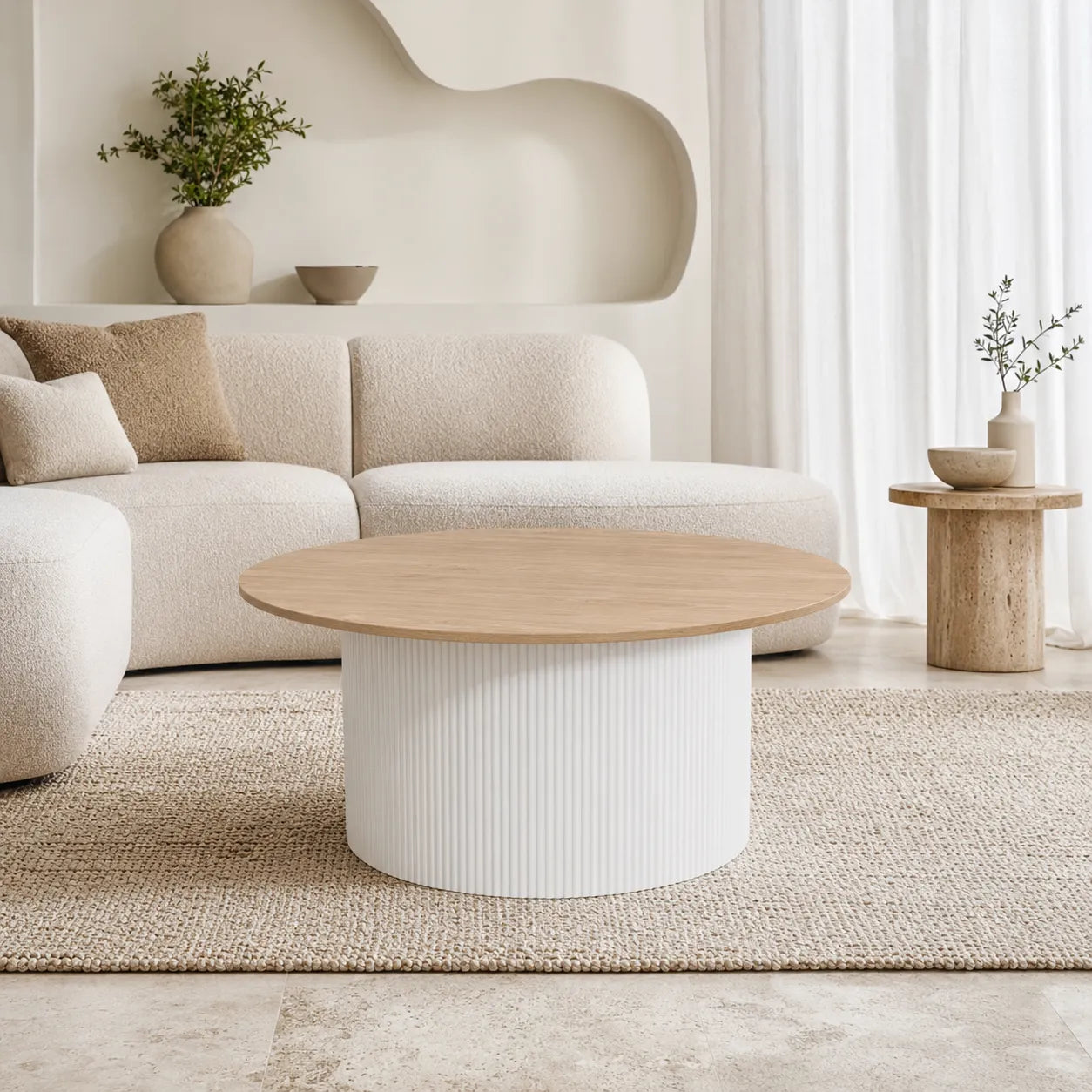 A modern round coffee table with a light natural wood top and a ribbed white cylindrical base, styled in a minimalist living room next to a beige sofa.