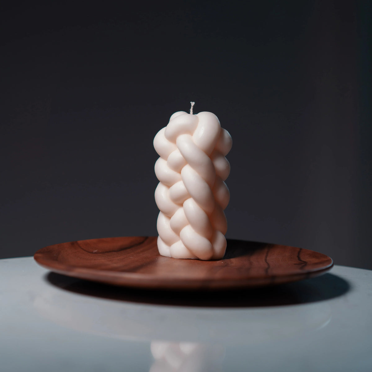 Braided candle on a wooden plate with a dark background