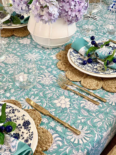 Table setting with floral tablecloth, plates, cutlery, and decorative elements.