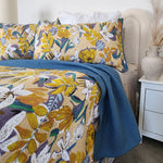 Floral bedding set with blue throw on a bed in a bedroom setting.