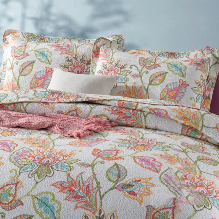 Floral patterned bedding set with pink blanket on a bed.