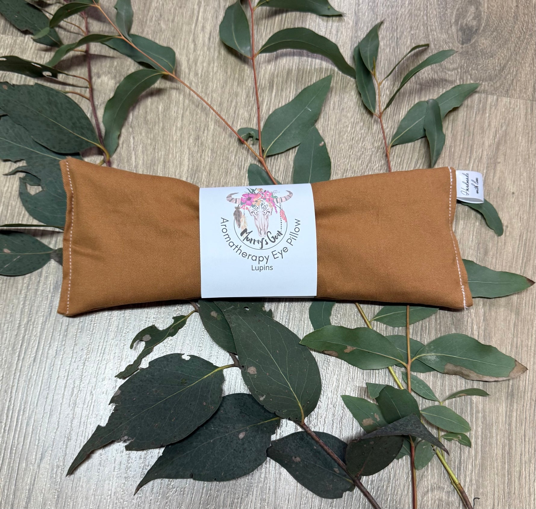 Brown eye pillow with a label on a wooden surface with eucalyptus leaves