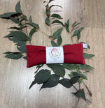 Red eye pillow with a label on a wooden surface with eucalyptus leaves