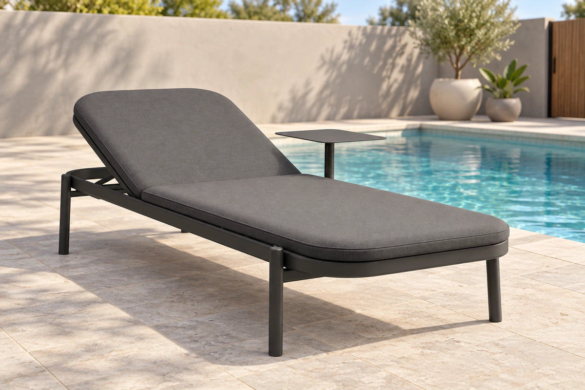 A modern outdoor chaise lounge chair with dark gray cushions and a black metal frame, positioned next to a swimming pool on a light stone patio.