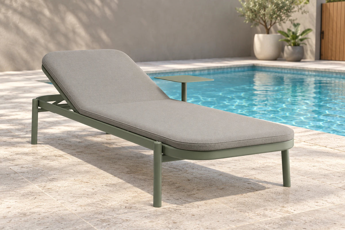 An outdoor chaise lounge with a light gray cushion and sage green metal frame, positioned next to a swimming pool on a stone patio.