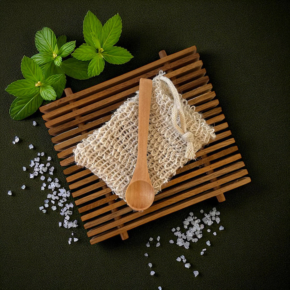 Wooden spoon on a woven mat with salt and mint leaves on a dark background